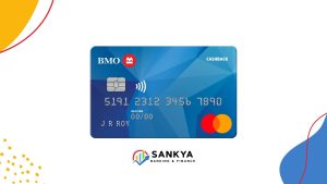 A BMO CashBack® Mastercard® credit card with a geometric blue background is displayed at the center. The card features embossed numbers, the name "J R Roy," and a contactless chip. The Mastercard logo appears in the bottom right. The background is white with colorful abstract shapes, and the Sankya Banking & Finance logo is centered below the card.