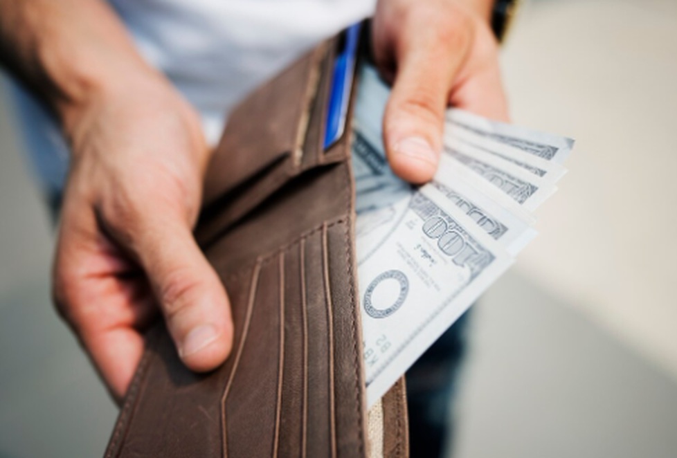A person holding a brown wallet and counting US dollar bills, illustrating the concept of cash stuffing and other trending spending control methods on social media.