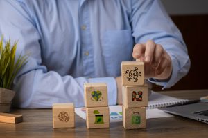 A person in a business shirt stacking wooden blocks with sustainability icons, symbolizing environmental, social, and governance practices, representing the growing focus on ESG in the U.S. and its impact on responsible investments.