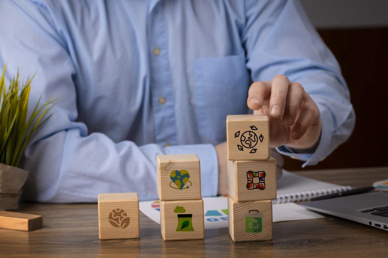 A person in a business shirt stacking wooden blocks with sustainability icons, symbolizing environmental, social, and governance practices, representing the growing focus on ESG in the U.S. and its impact on responsible investments.